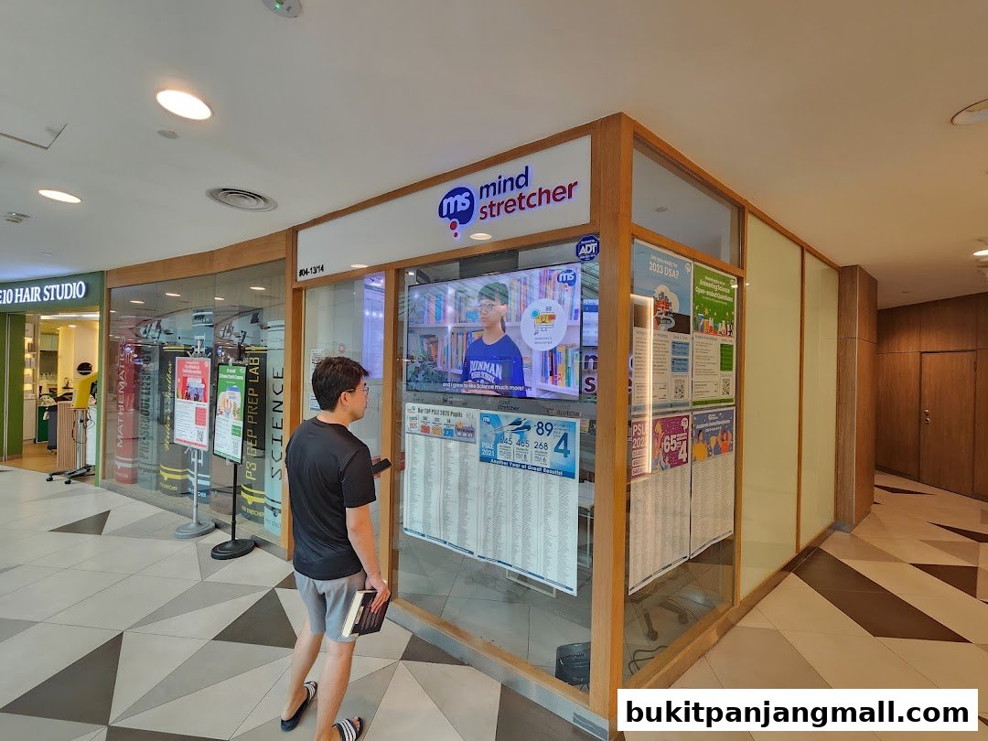 A man stands outside a Mind Stretcher tuition center, looking at a display board.