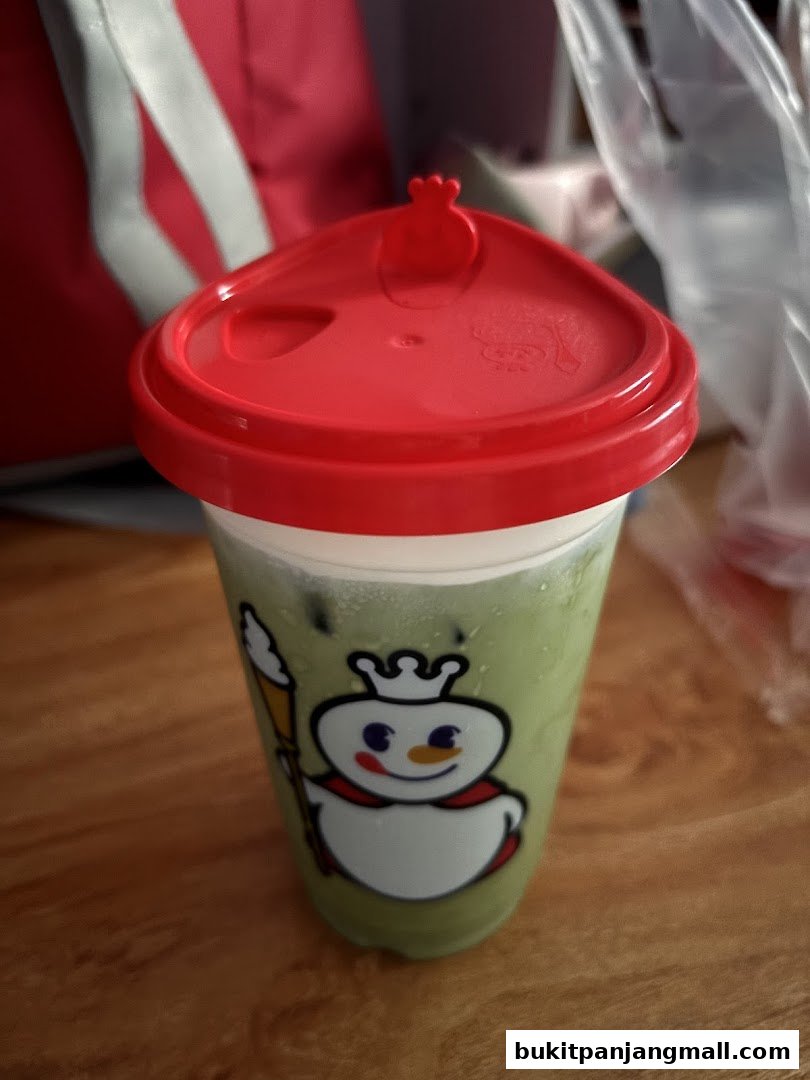 A close-up of a green beverage in a clear cup with a red lid, featuring the MIXUE logo.