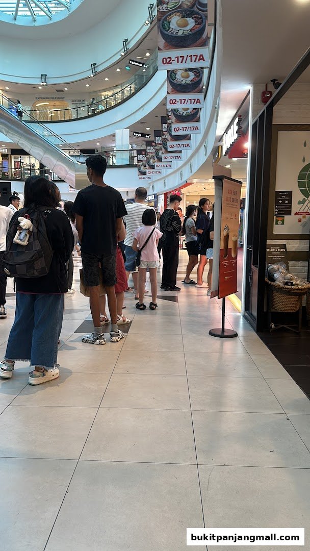 People queuing at a shop entrance in a mall, with food advertisements overhead.