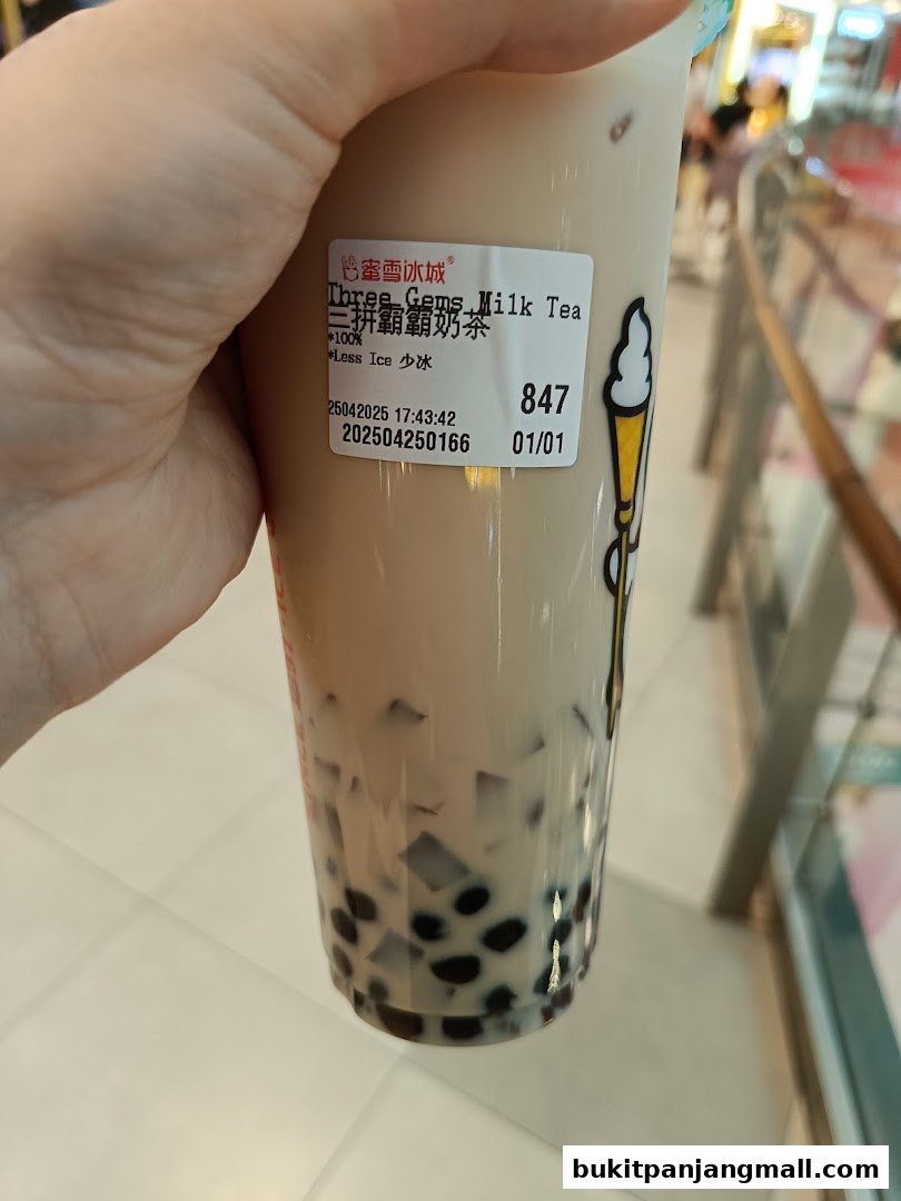 A hand holds a cup of bubble tea with a label indicating 'Three Gems Milk Tea'.