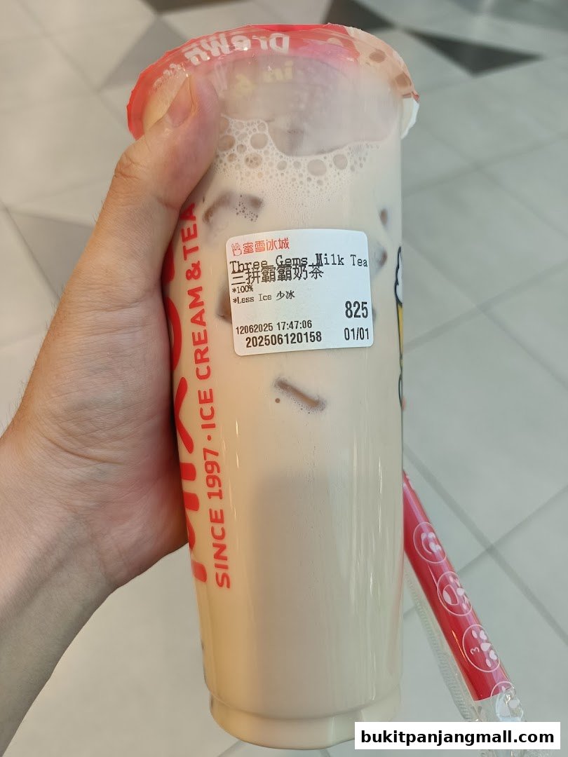 A hand holds a cup of milk tea with a label showing the product name and details.