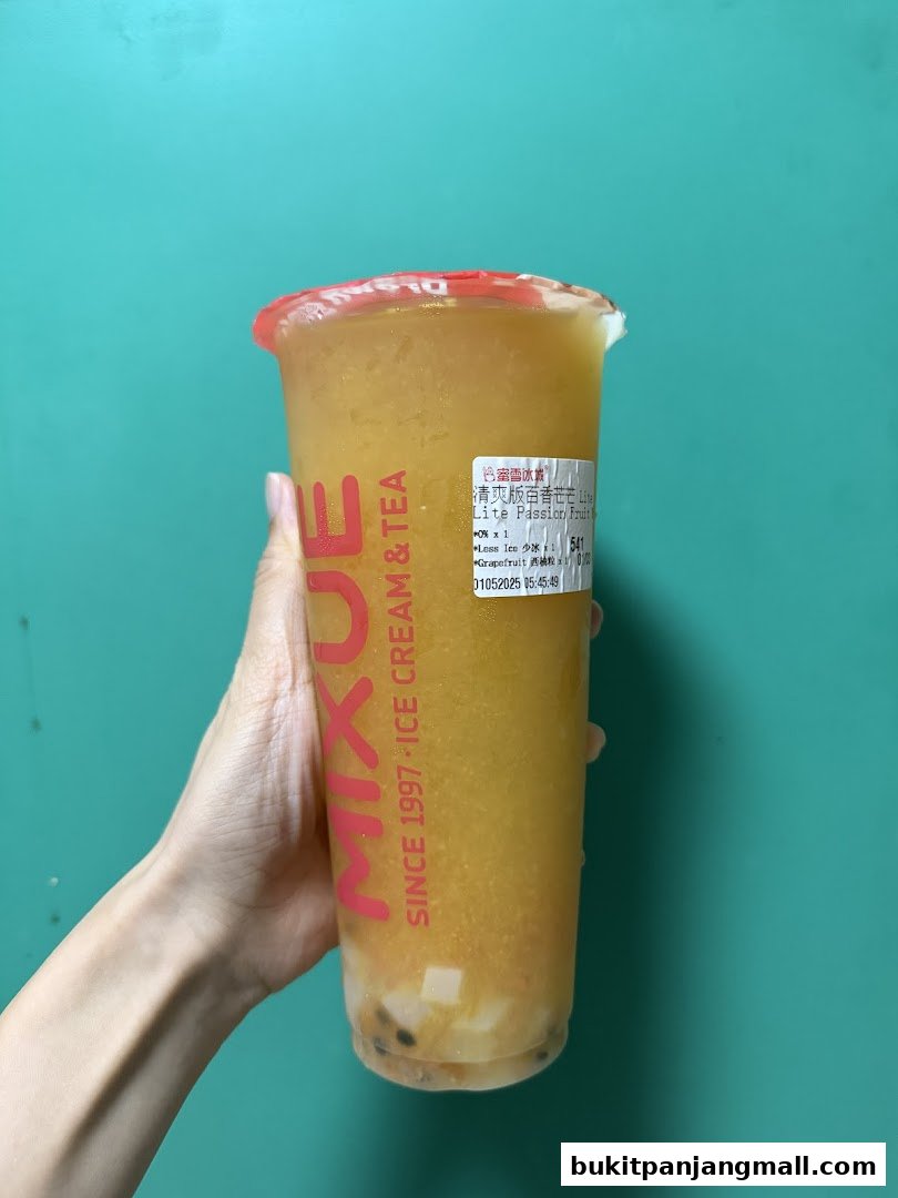 A hand holds a large cup of yellow slushy drink with fruit pieces and boba.