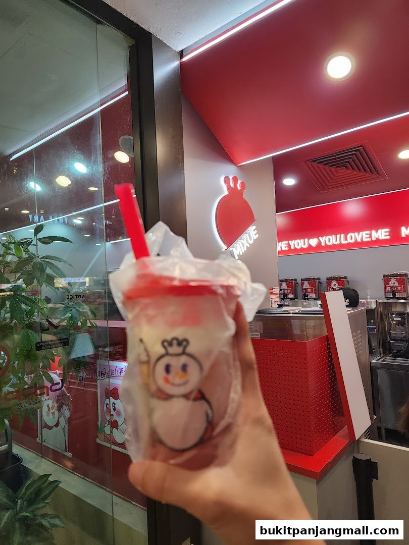 A hand holds a packaged drink with a snowman logo in front of a Mixue store.