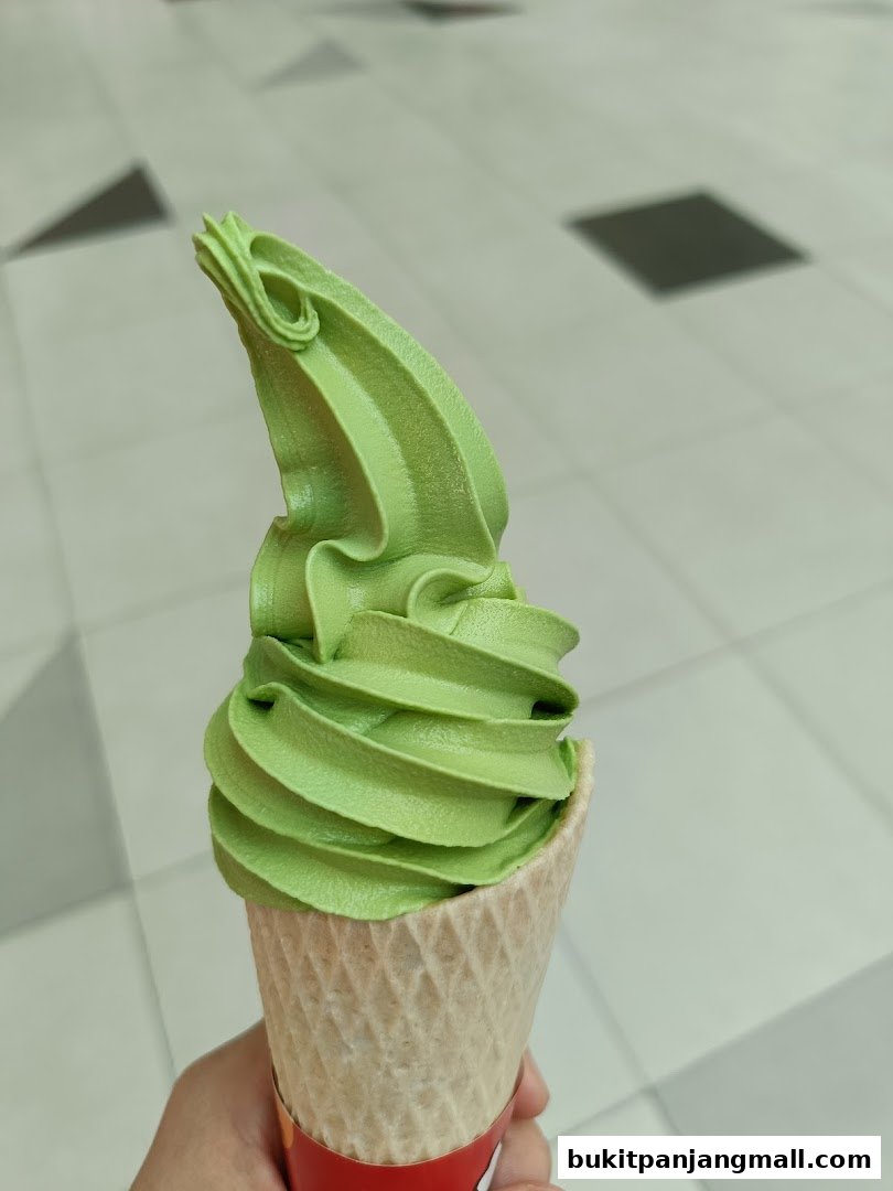A hand holds a green soft-serve ice cream cone with a waffle cone.