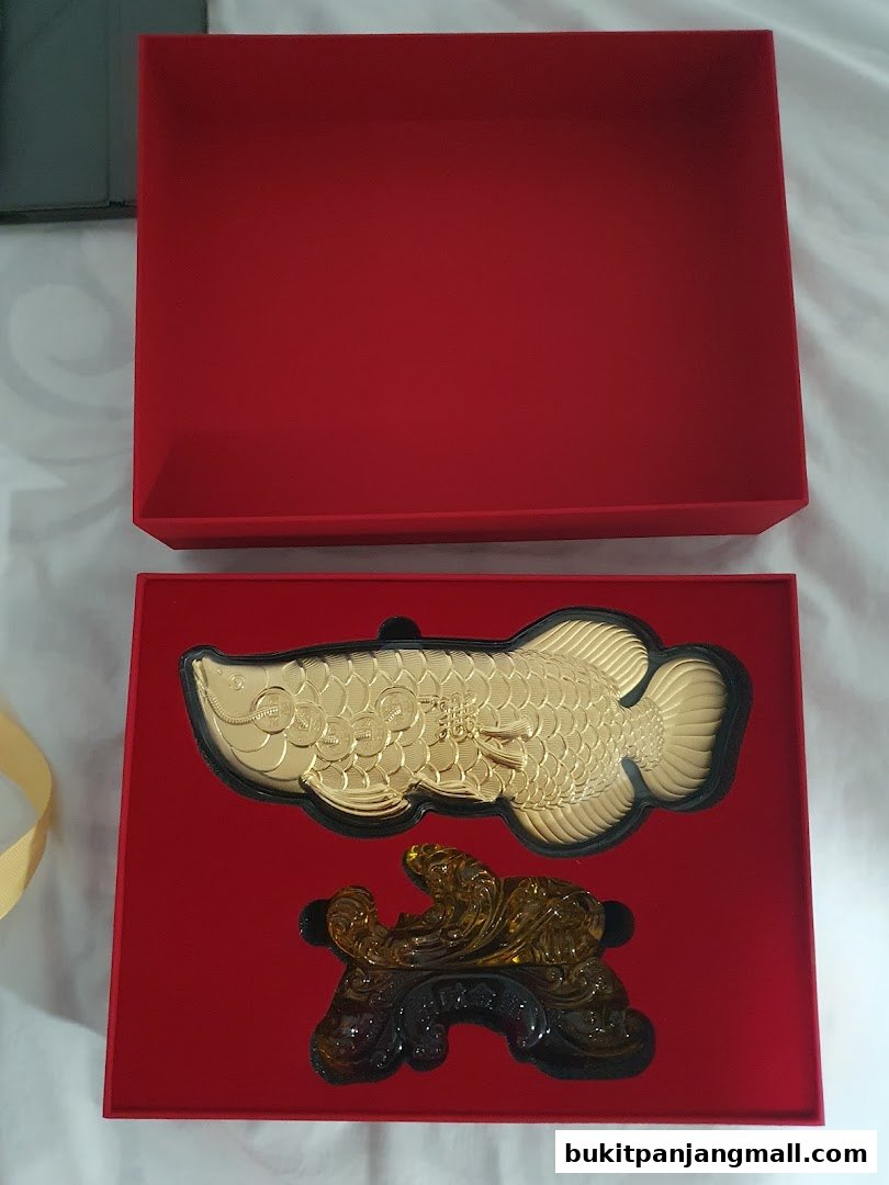 A gold Arowana fish ornament and a crystal dragon figurine in a red gift box.