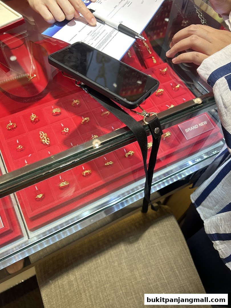 Close-up of a jewelry display case with gold rings and a customer reviewing paperwork.