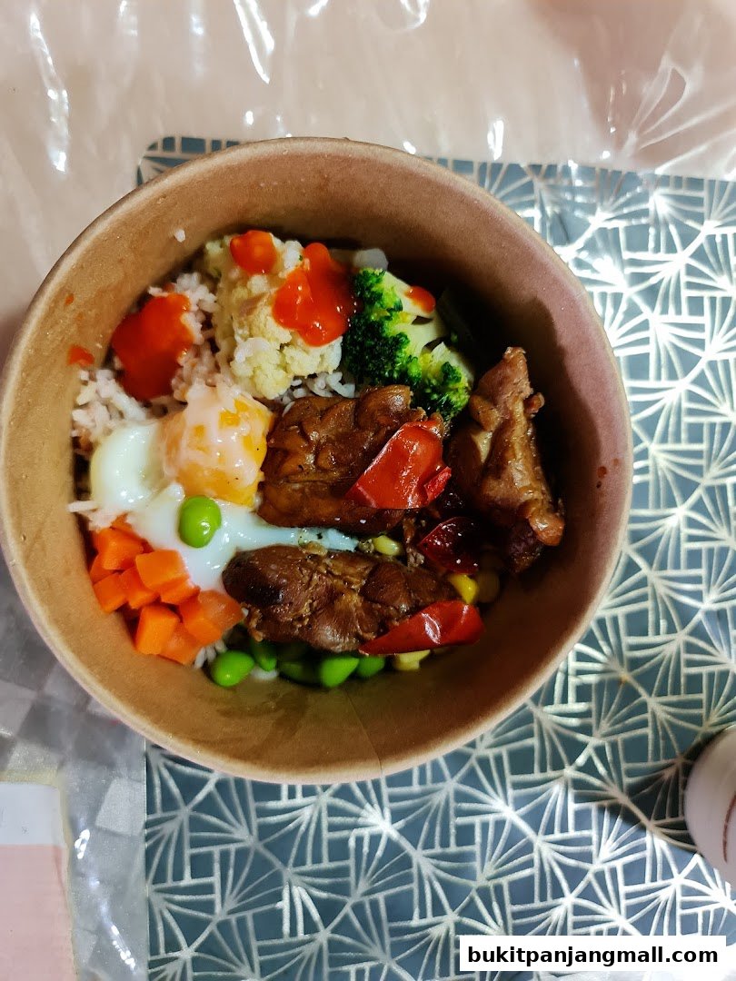 A delicious bowl of rice with chicken, vegetables, and a fried egg, drizzled with sauce.