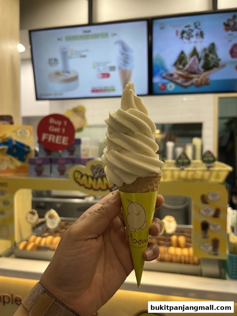A hand holds a soft-serve ice cream cone in front of a shop display.