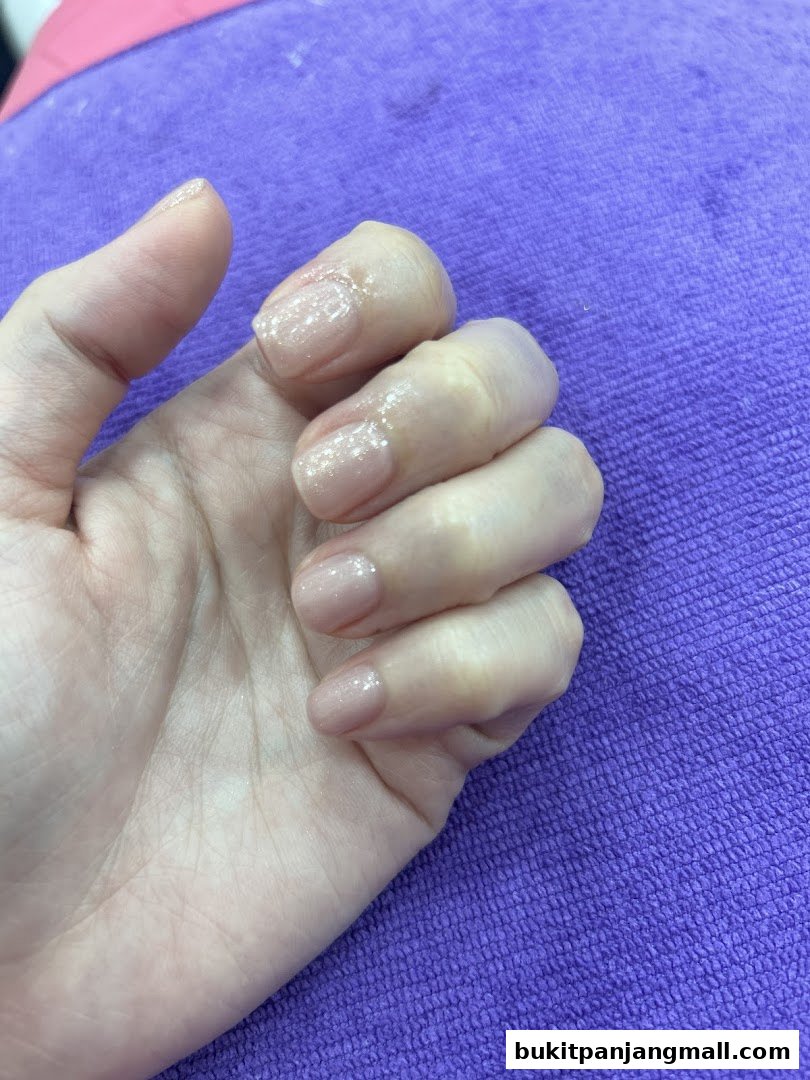 A close-up of a hand with neatly manicured nails, featuring a subtle glitter polish.