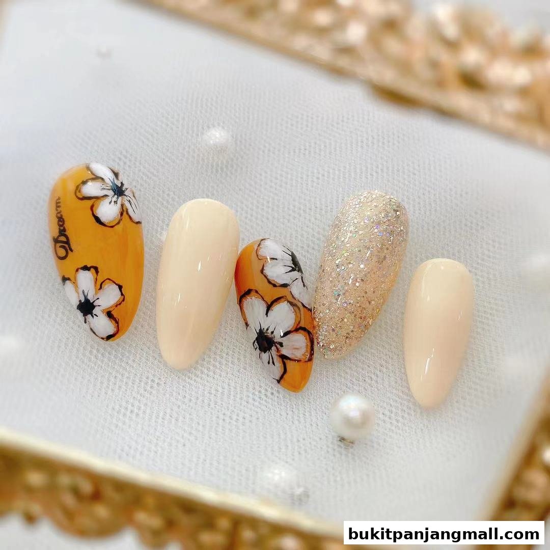 A display of five artificial nails, some with floral designs and glitter, on a white cloth.