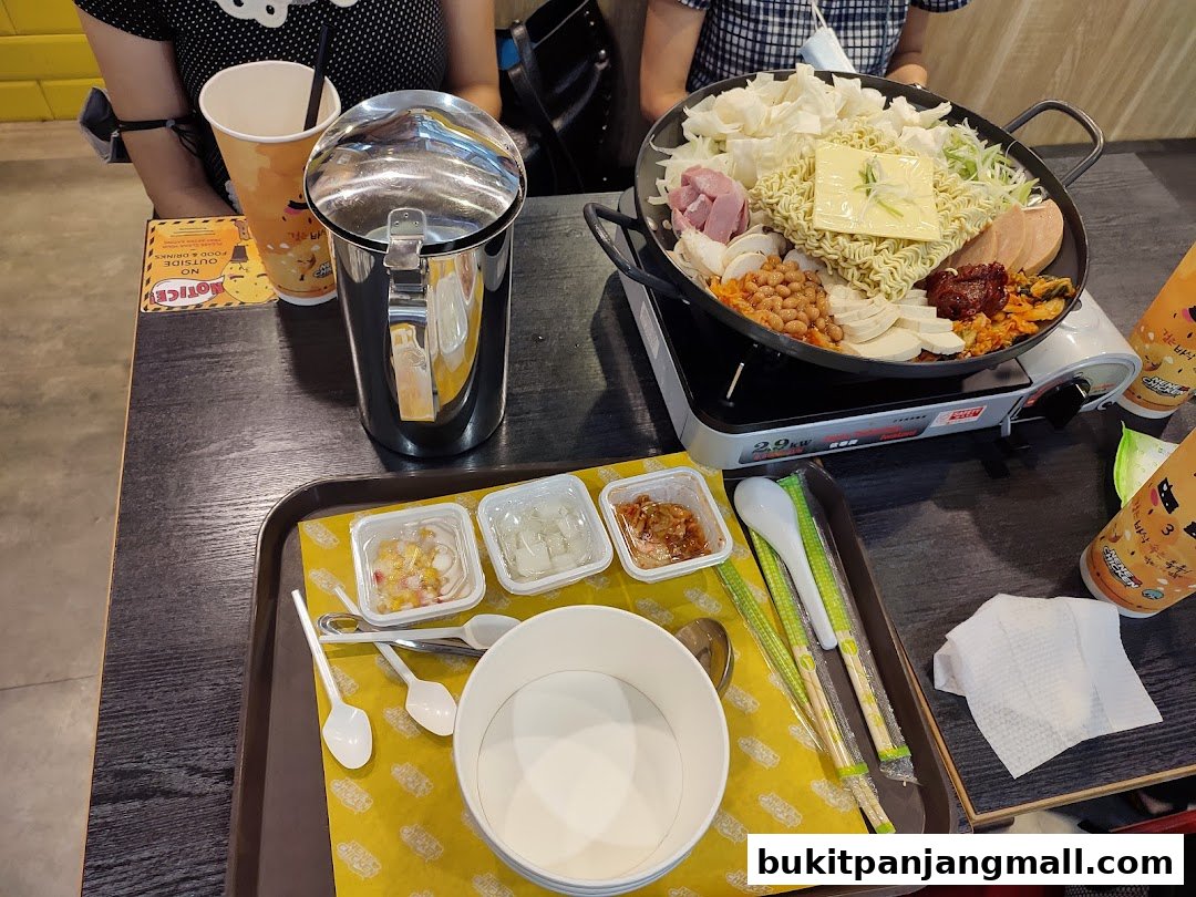 A table setting with a hot pot dish, drinks, and condiments at NeNe Chicken.