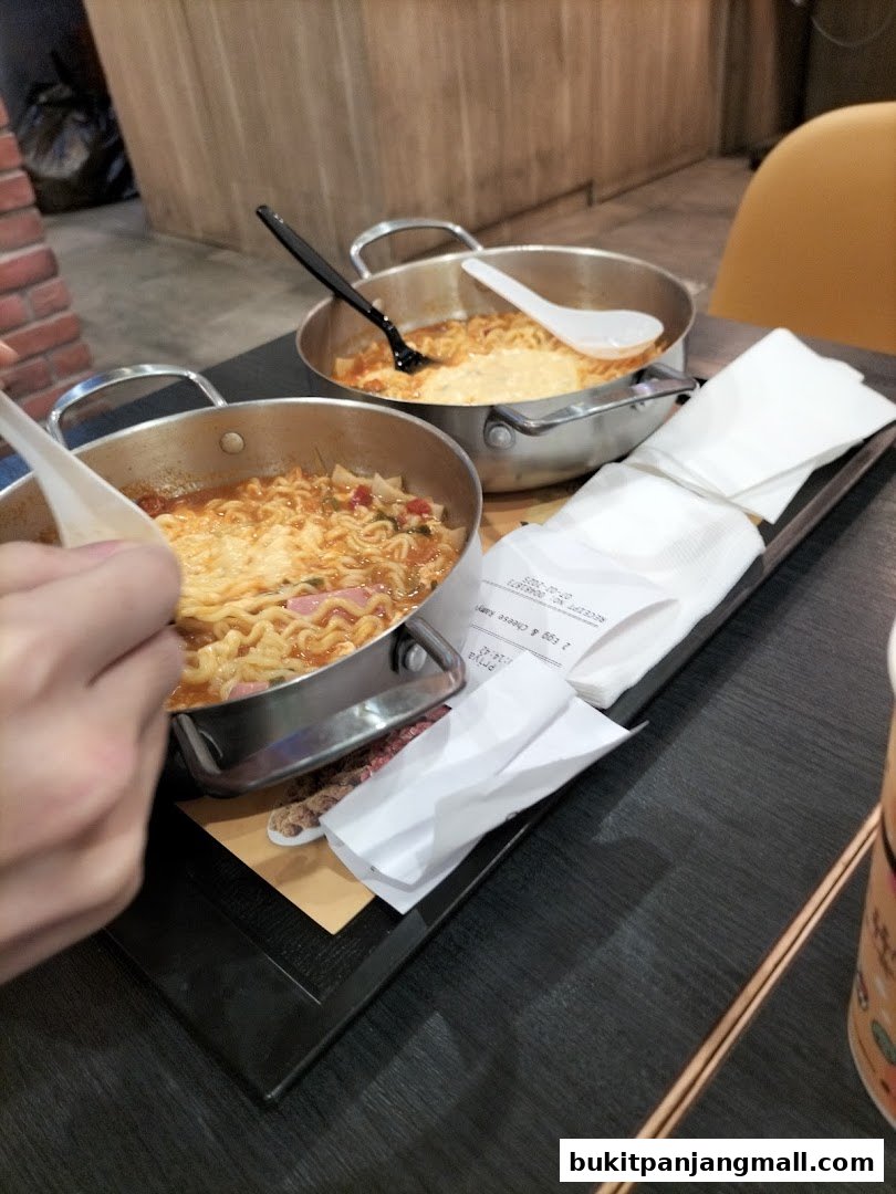 Two steaming bowls of ramen with melted cheese, served with napkins and cutlery.