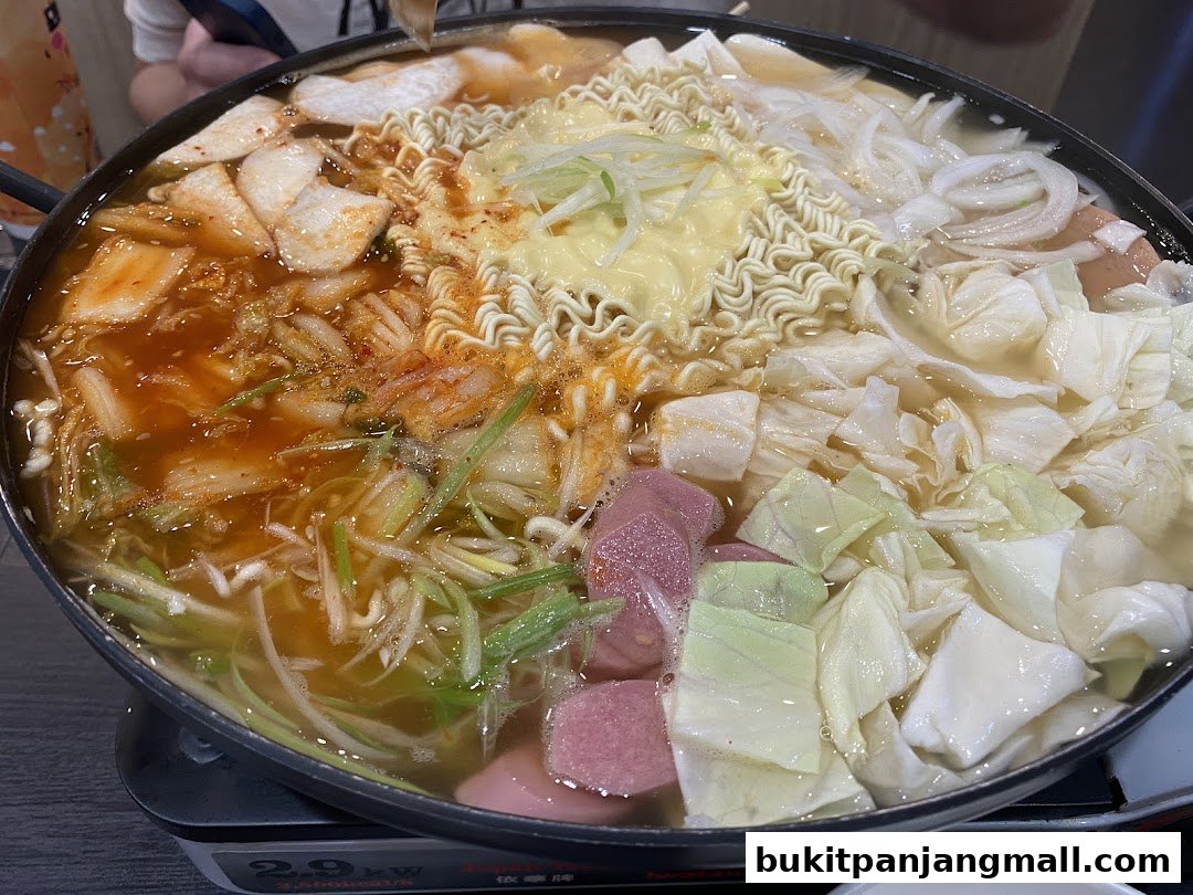 A bubbling hot pot filled with kimchi, noodles, cabbage, and sausages.