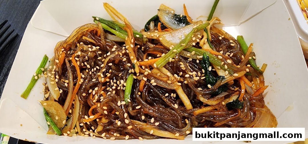 A close-up of a delicious Korean Japchae dish with noodles, vegetables, and sesame seeds.