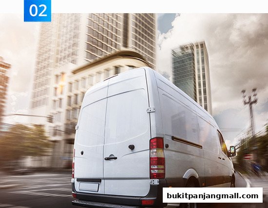 A white delivery van driving on a city street with blurred buildings in the background.