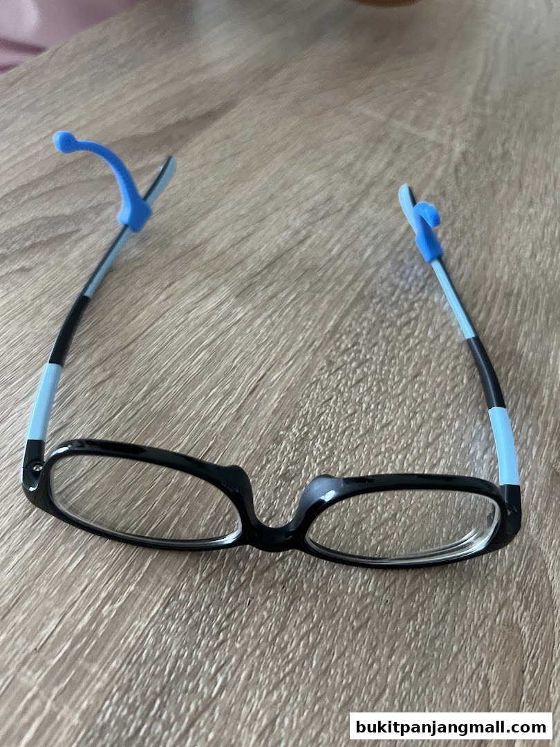 A pair of black eyeglasses with blue ear hooks rests on a wooden surface.