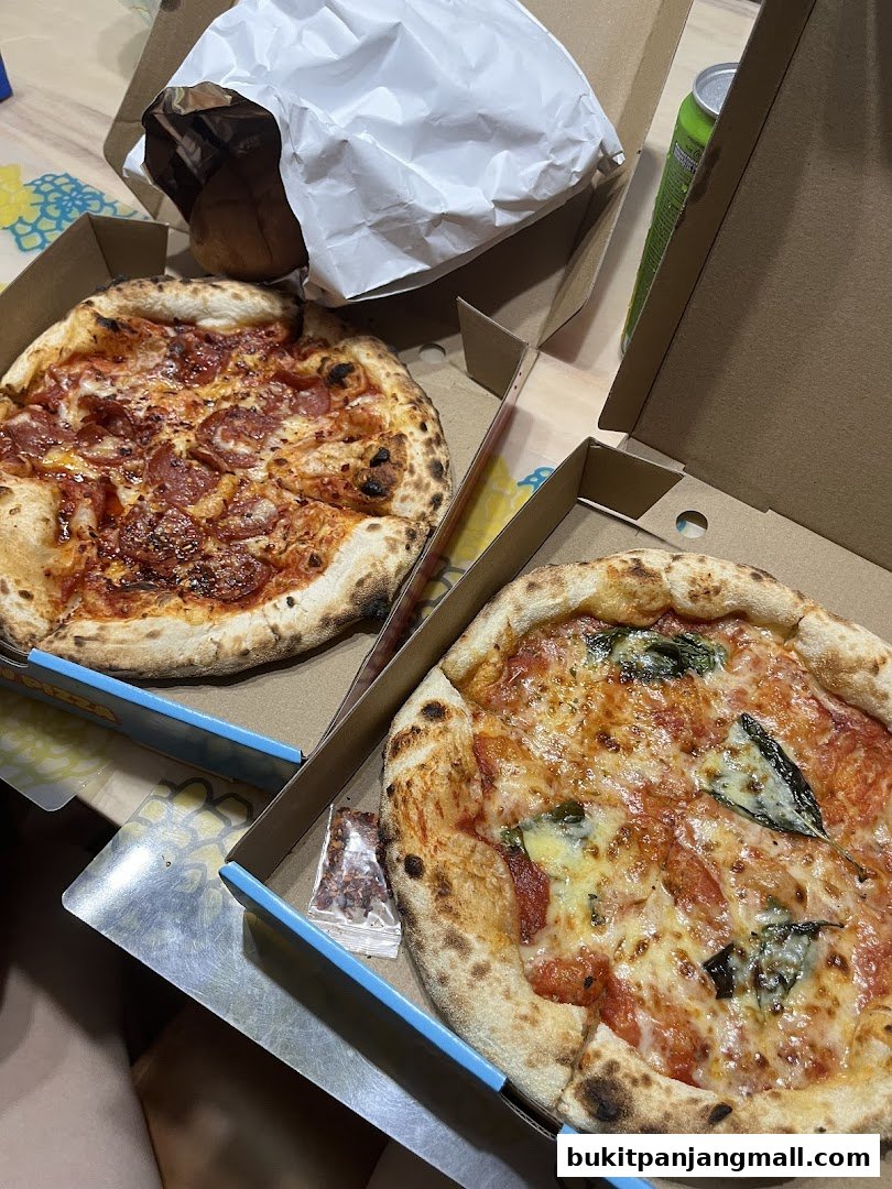 Two delicious pizzas, one with pepperoni and the other with basil, in their boxes.