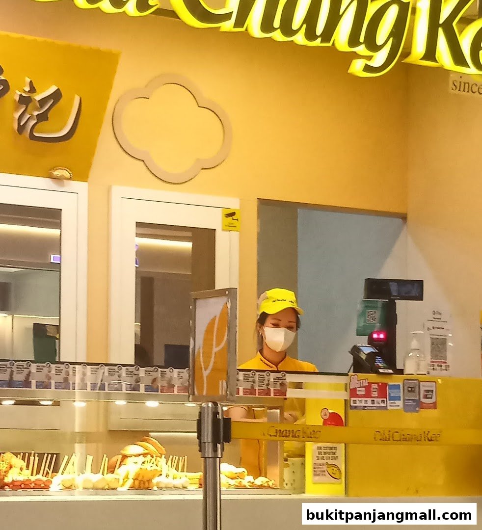 A staff member wearing a mask and yellow cap stands behind the counter at Old Chang Kee.