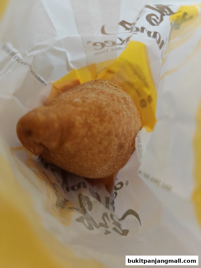 A close-up shot of a golden-brown pastry inside a white and yellow Old Chang Kee paper bag.
