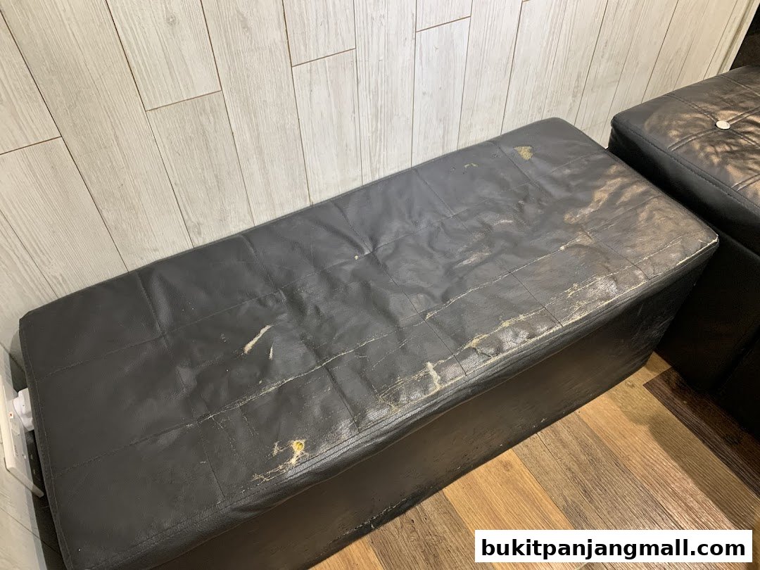 A worn black leather ottoman with visible damage and scuff marks.
