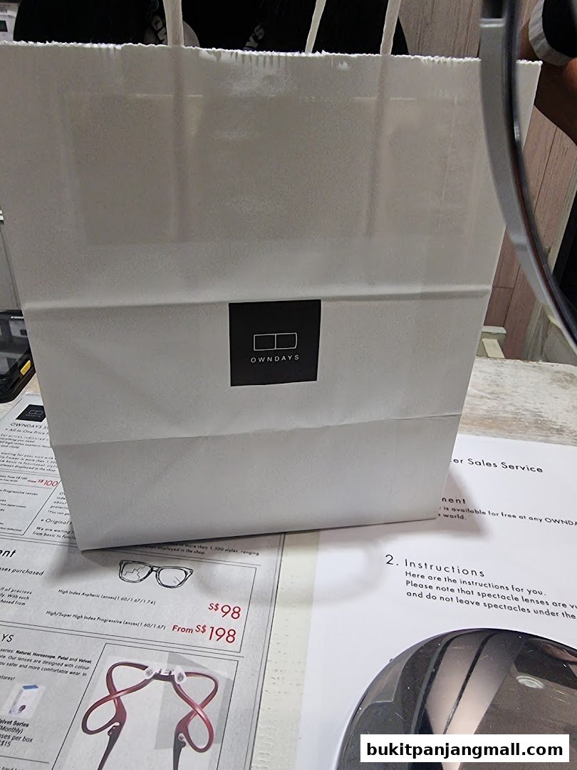 A white shopping bag with the OWNDAYS logo sits on a table with optical product information.