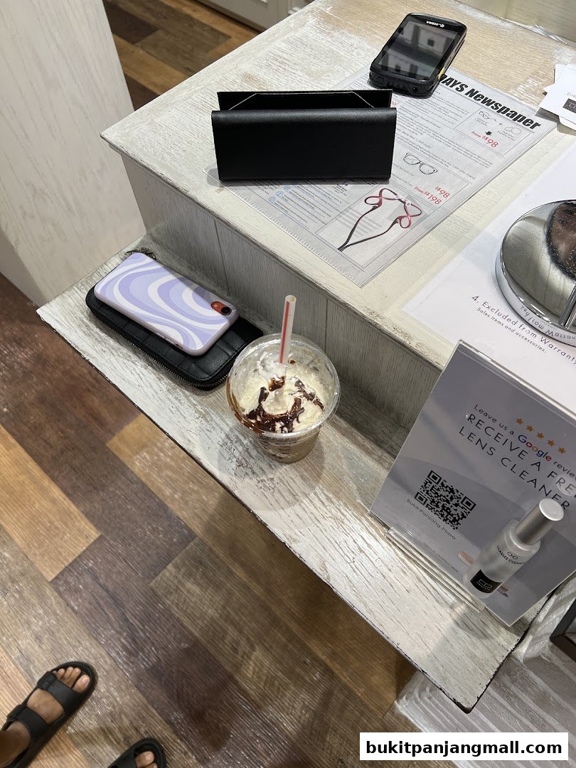 A counter with a phone, glasses display, and a drink at an optical shop.