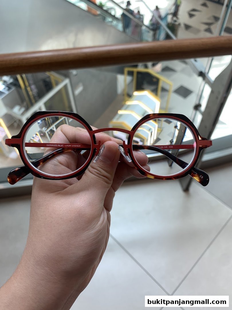A hand holds a pair of stylish red and tortoiseshell eyeglasses with clear lenses.