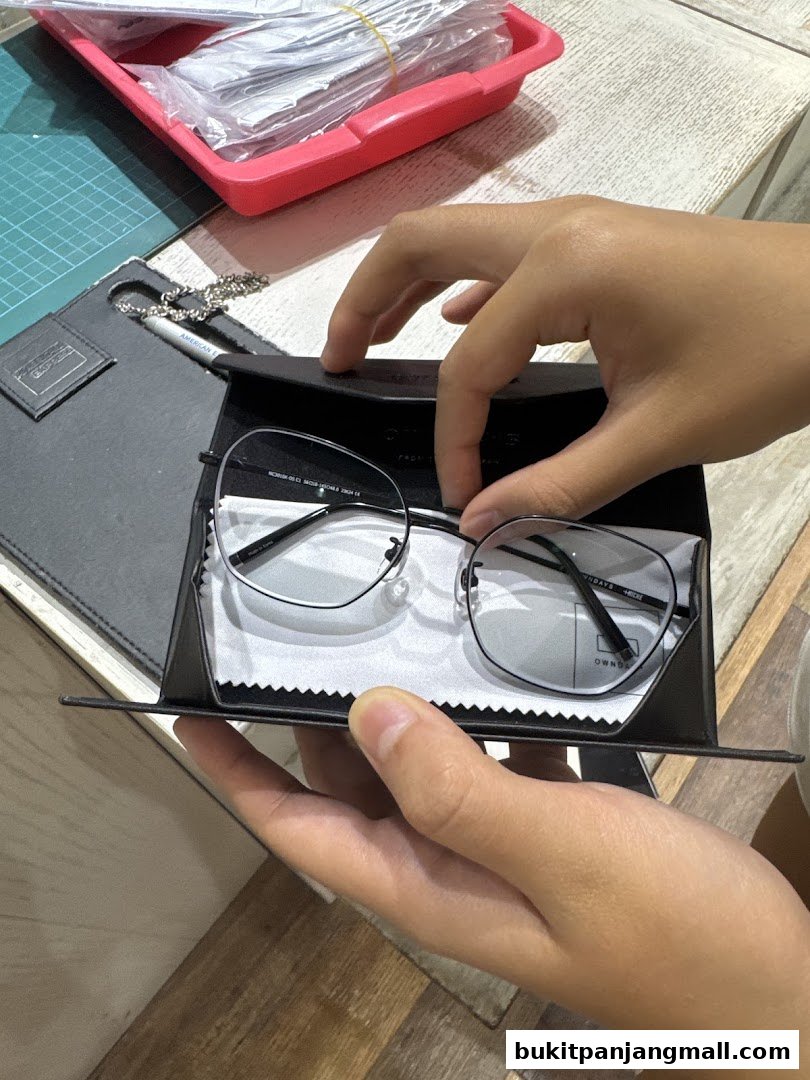 Hands holding a pair of modern eyeglasses in a black case with a cleaning cloth.