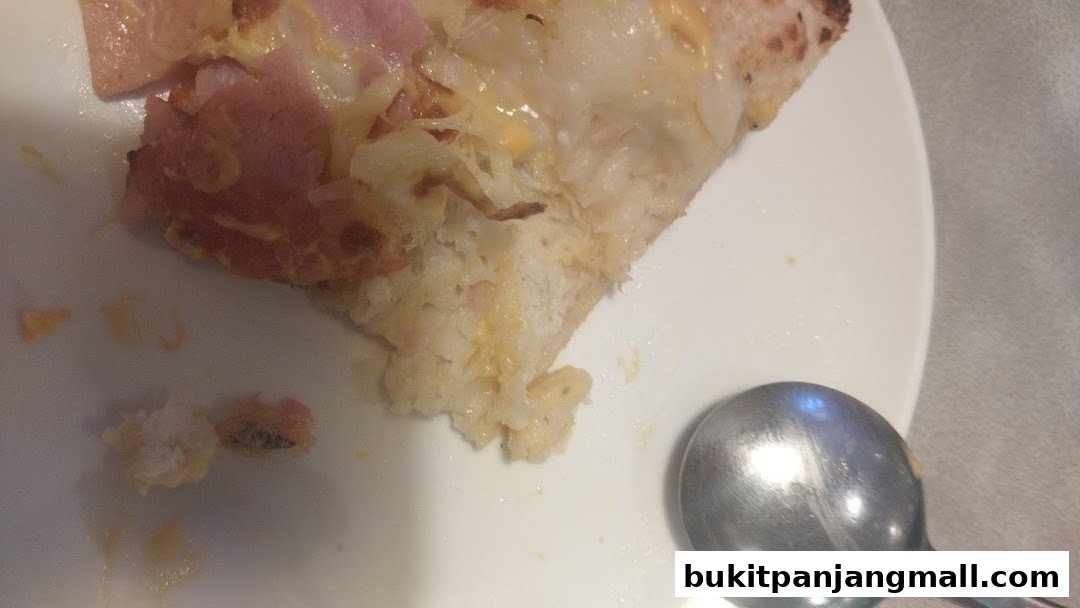 A close-up shot of a slice of pizza with ham and cheese on a white plate with a spoon.