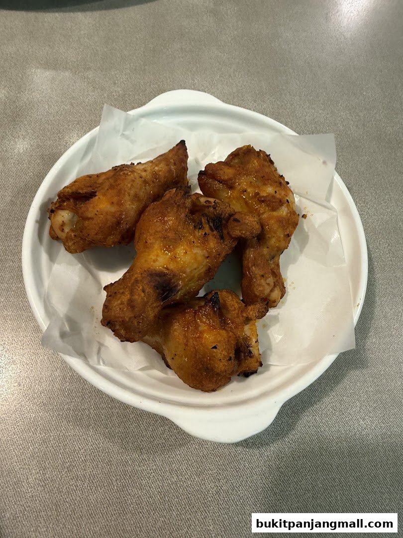 A white bowl filled with four golden-brown chicken wings seasoned with spices.