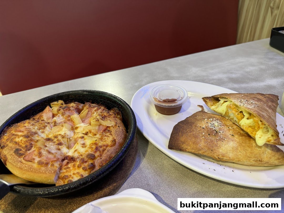 A delicious Hawaiian pizza and a cheesy calzone are served on a table at Pizza Hut.