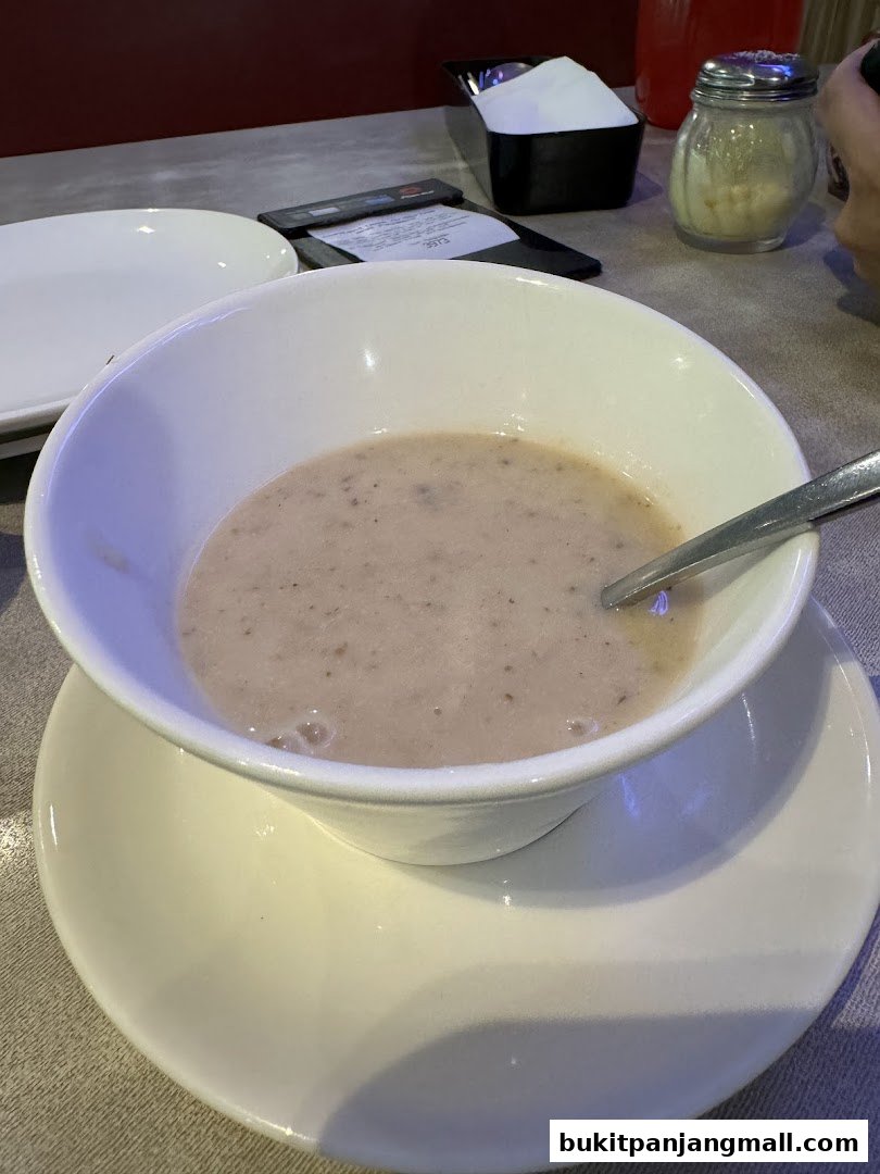 A bowl of creamy mushroom soup served with a spoon on a table.