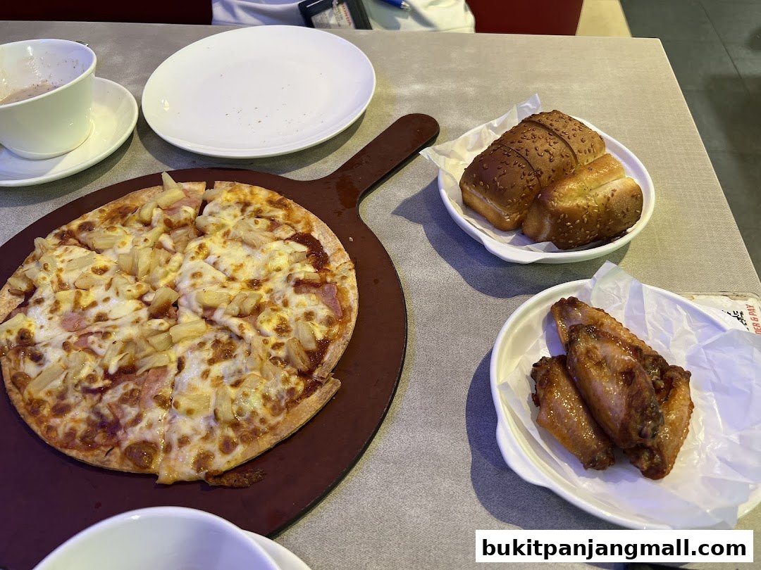A table setting with a pizza, chicken wings, bread rolls, and a drink.