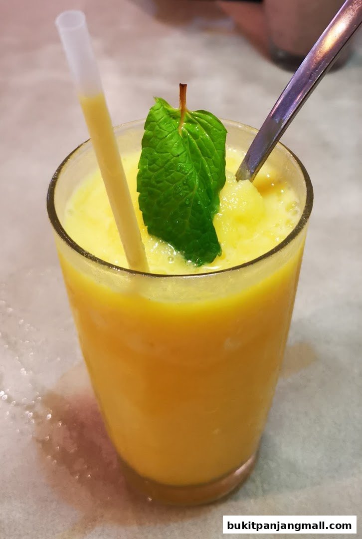 A refreshing yellow smoothie topped with a mint leaf and served with a straw and spoon.