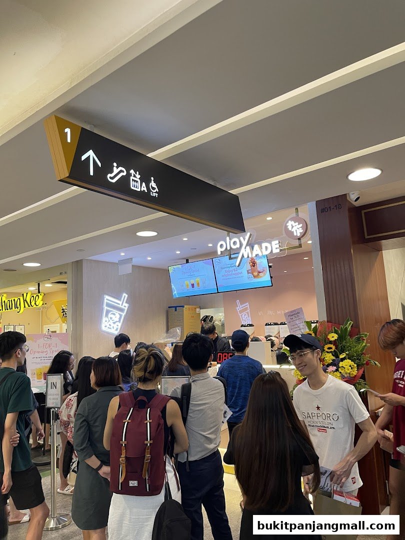 A queue of people waiting outside a PlayMade bubble tea shop with a promotional sign.