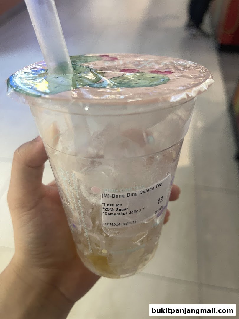A hand holds a nearly empty cup of bubble tea with ice and some jelly.