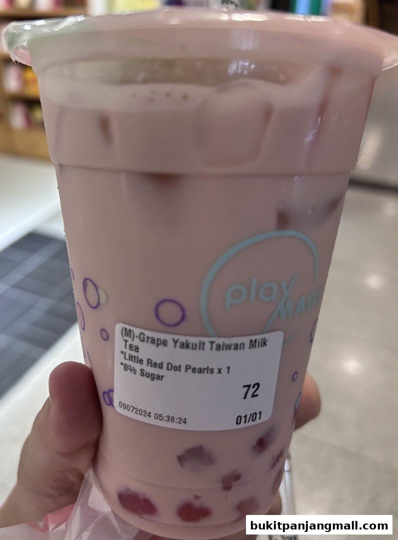 A hand holds a pink grape yakult taiwan milk tea with red pearls and 0% sugar.