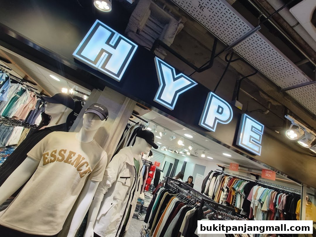 A clothing store interior with mannequins and racks of apparel under a large illuminated sign.