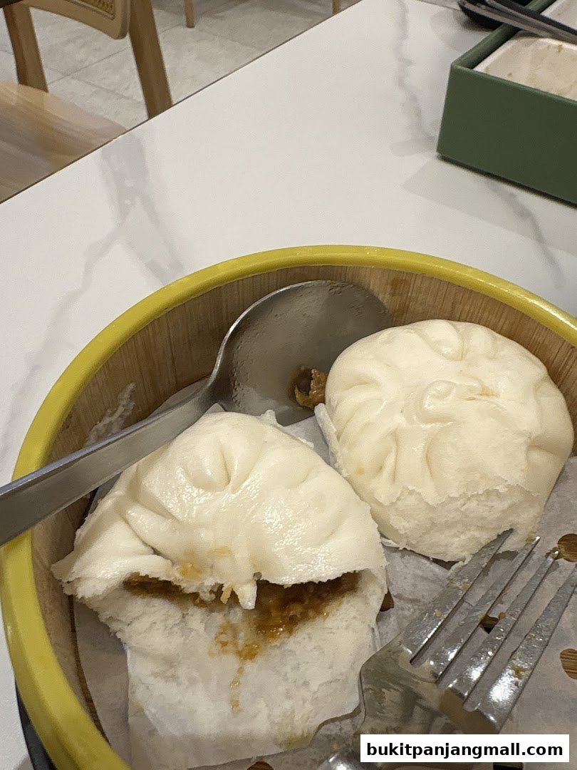 A close-up shot of two steamed buns in a bamboo steamer basket with a fork and spoon.