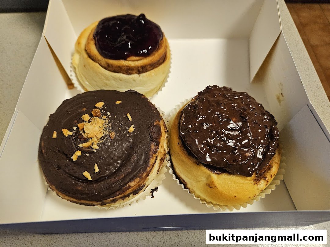 Three freshly baked cinnamon rolls with different toppings in a white box.