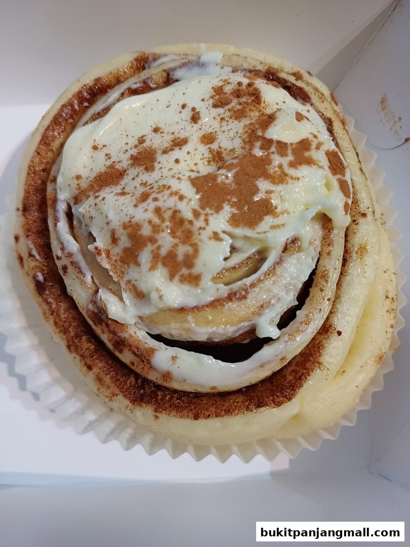 A close-up shot of a freshly baked cinnamon roll topped with cream cheese frosting and cinnamon.