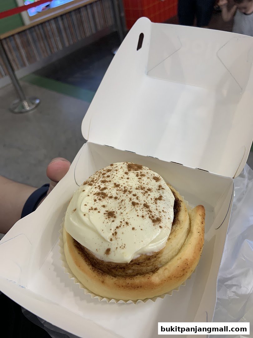 A close-up of a cinnamon roll with cream cheese frosting and cinnamon powder in a white box.