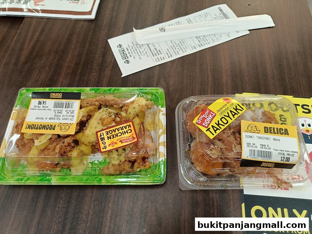 Two pre-packaged Japanese dishes, Chicken Karaage and Takoyaki, are displayed on a wooden surface.