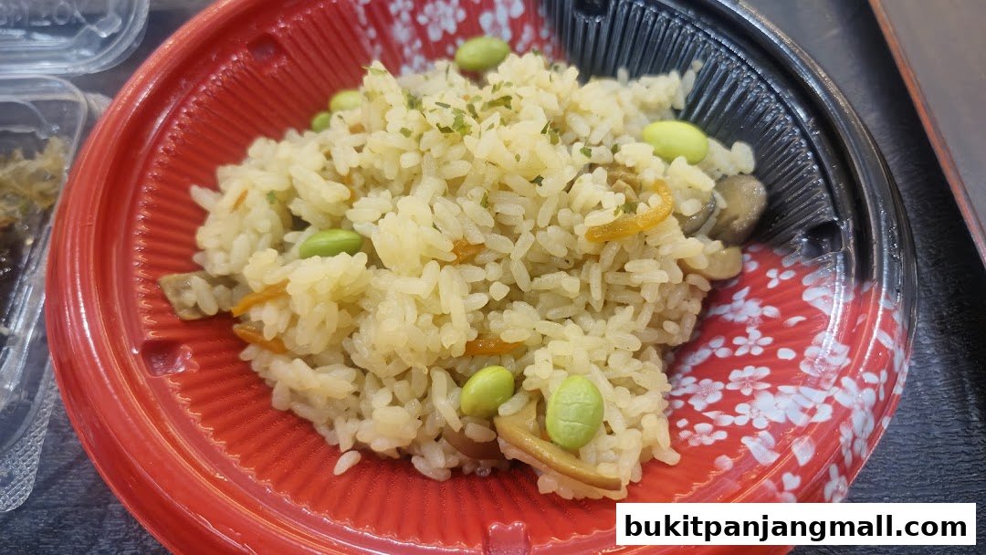 A close-up of a takeaway rice dish with edamame beans and mushrooms in a red plastic container.