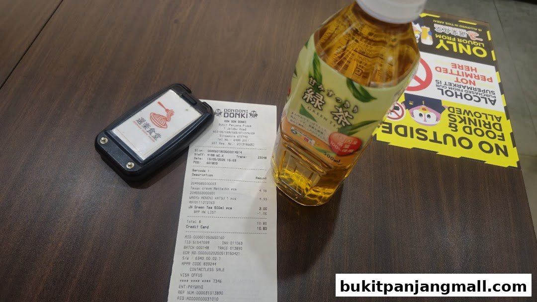 A receipt and a bottle of green tea on a wooden table, with a sign in the background.