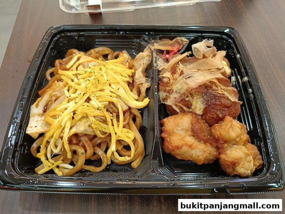 A bento box with noodles, fried chicken, and takoyaki topped with bonito flakes.