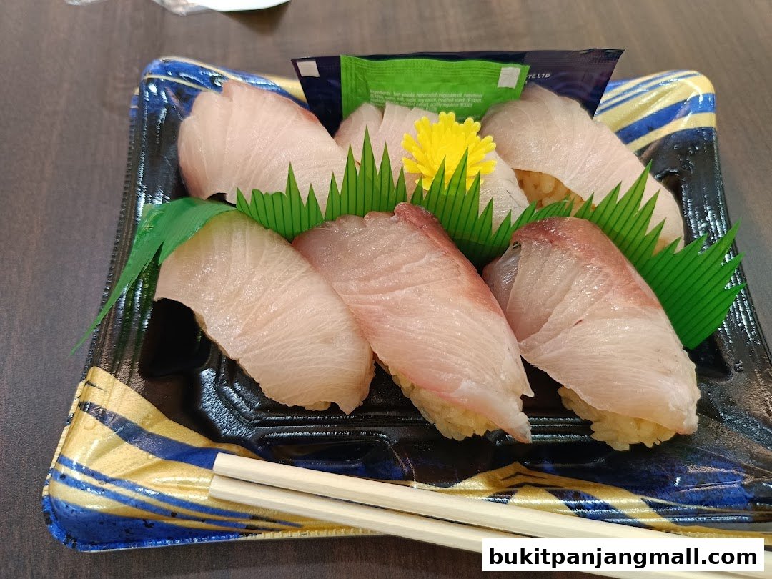A take-out container filled with fresh sushi, garnished with green leaves and a yellow flower.