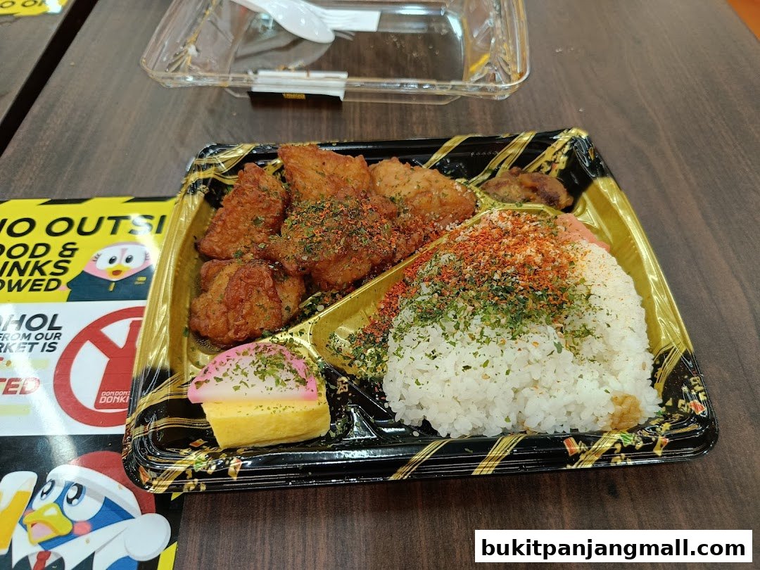 A bento box with fried chicken, rice, and tamagoyaki on a wooden table.