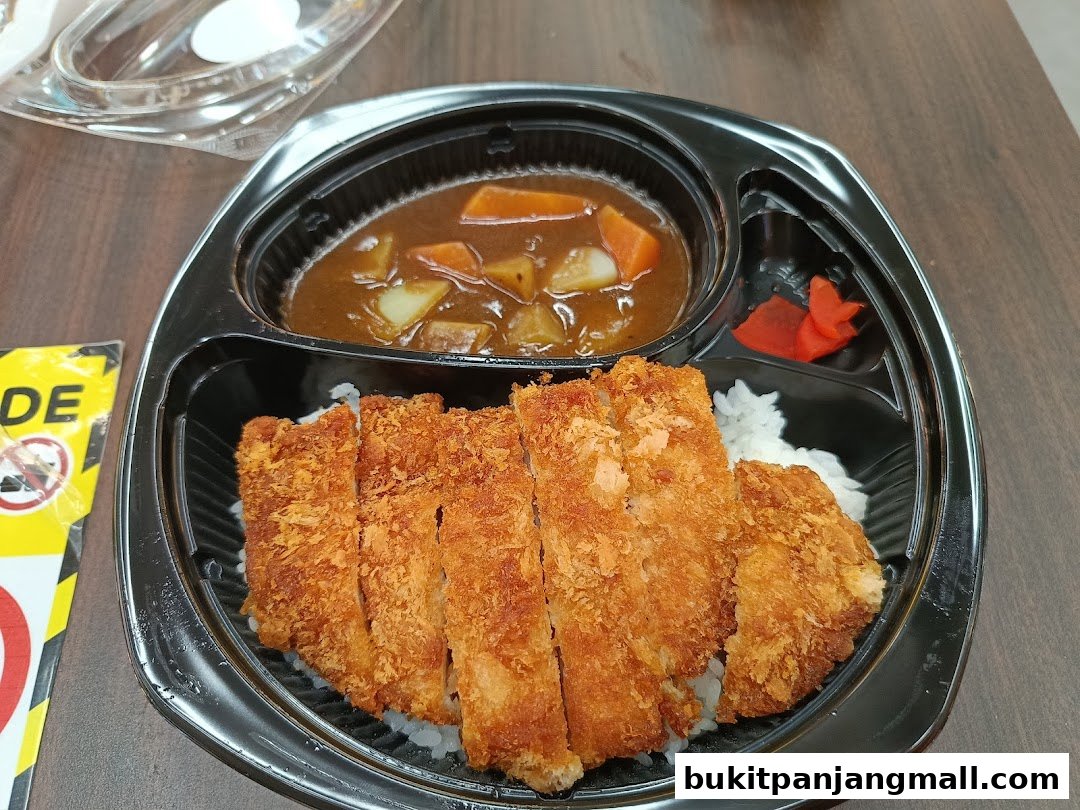 A bento box with crispy fried pork cutlet, rice, curry, and pickled ginger.