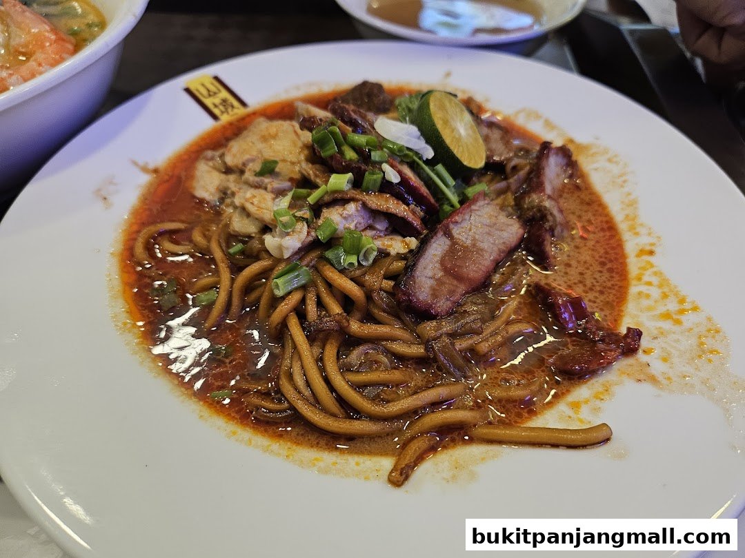 A plate of Ipoh noodles with sliced roasted meat and garnished with spring onions and lime.